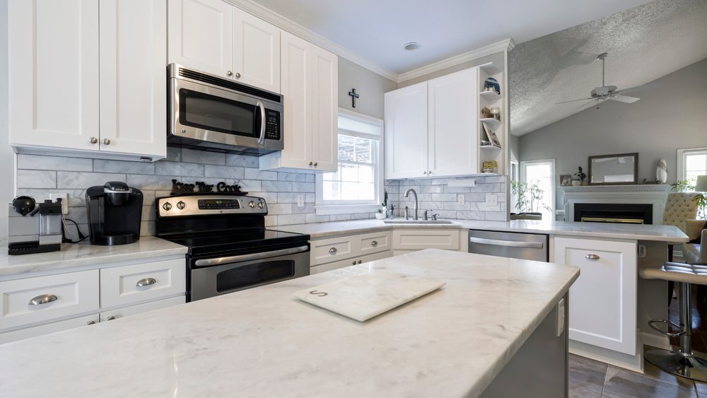 White kitchen with a marble island opening onto the living room